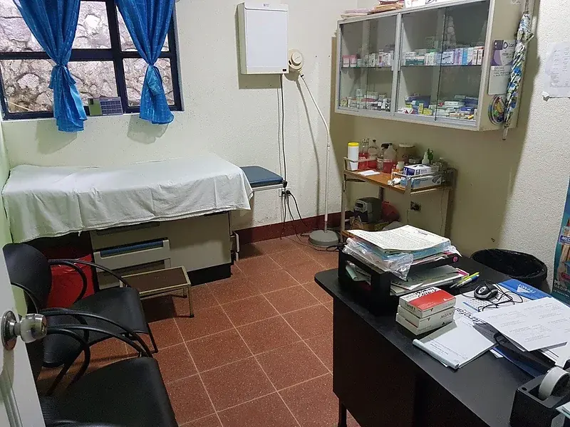 Ein Ambulanzraum mit Untersuchungsliege, Schreibtisch und Medikamentenregal