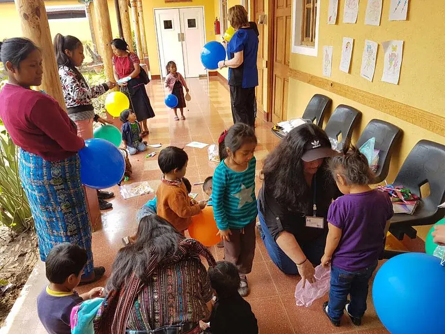 Kinder spielen mit Luftballons, Betreuerinnen knien dazwischen