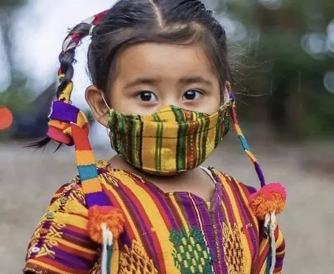 Ein Mädchen in traditioneller Kleidung mit bunt gewebter Maske